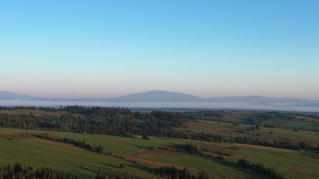 Aerial footage showing Babia Gora mountain seen from Podhale region with forest and fields under clear morning sky