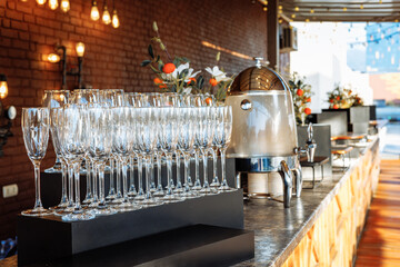 Gleaming glassware lined up next to a thermal carafe against rustic brick and floral decor - ideal for upscale catering or luxury venue branding.