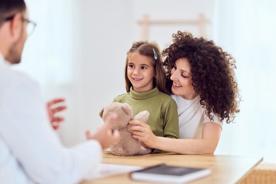 Mother And Daughter Visit Doctor's Office For Checkup With Teddy Bear And Warm Smile Together