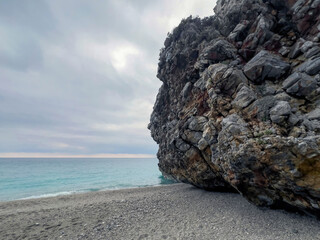 Majestic rock formation by serene beach overlooking calm ocean waters at dusk