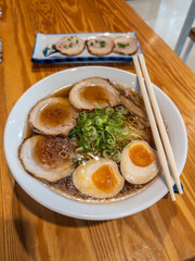 A steaming bowl of authentic Japanese ramen, featuring rich pork broth, tender chashu slices, perfectly marinated ajitama eggs, springy noodles, and fresh scallions, served on a rustic wooden table.