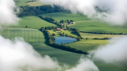 Aerial view of green farmland fields and small lake framed by clouds