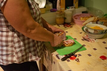 Slicing ham for sandwich, cozy kitchen setting. Woman preparing food with a homey feel, making a...