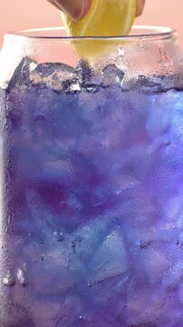 Close-up footage of a hand squeezing lemon juice into a glass of Thai blue butterfly pea tea "Anchan" with ice. The color of the drink changes from blue to purple