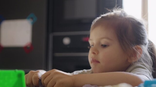 young girl with playful interest touching slimy purple material under bright kitchen lighting