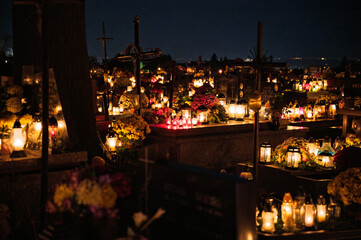 Night scene of a cemetery illuminated by hundreds of candles during All Saints Day. Warm glowing lights, bokeh and flowers creating a peaceful, spiritual atmosphere. Shot in Biały Kościół, Poland.