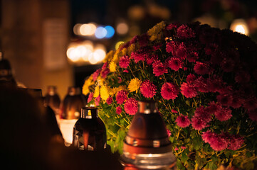 Night scene of a cemetery illuminated by hundreds of candles during All Saints Day. Warm glowing lights, bokeh and flowers creating a peaceful, spiritual atmosphere. Shot in Biały Kościół, Poland.