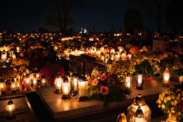 Night scene of a cemetery illuminated by hundreds of candles during All Saints Day. Warm glowing lights, bokeh and flowers creating a peaceful, spiritual atmosphere. Shot in Biały Kościół, Poland.