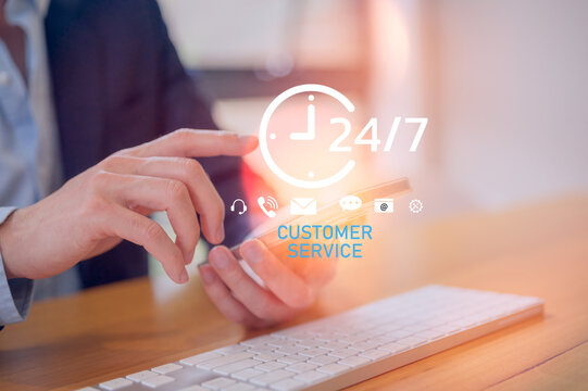 Close-up of businessman using smartphone and keyboard with 24/7 customer service icons, symbolizing online communication, technical support, help desk, and professional client assistance.