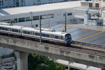 A sleek train moves steadily along an elevated railway in a bustling city, showcasing a blend of...