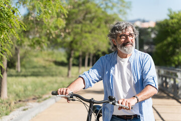 Happy retired man walking with his bicycle in a city park on a sunny day