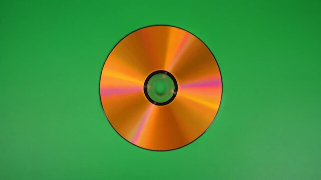 Single compact disc with orange reflective surface and pink-purple diffraction streaks against solid green background, evoking digital nostalgia, optical beauty, and minimalist tech symbolism.