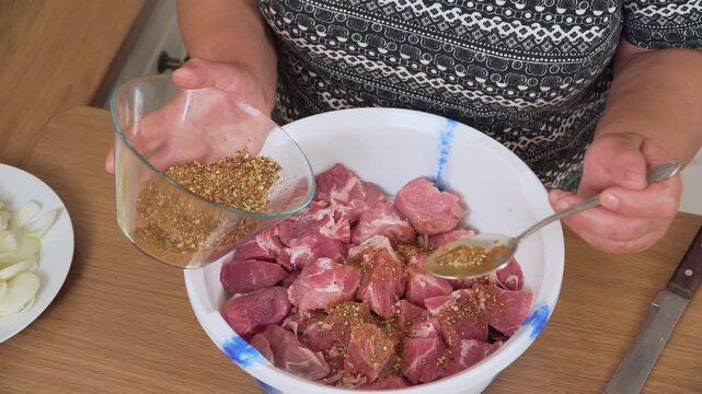 Sprinkling spice mix over pork chunks in bowl. Unrecognizable person seasoning meat for outdoor grilling. Adding aromatic herbs to enhance marinade flavor. Cooking dish marinated shashlik skewers for