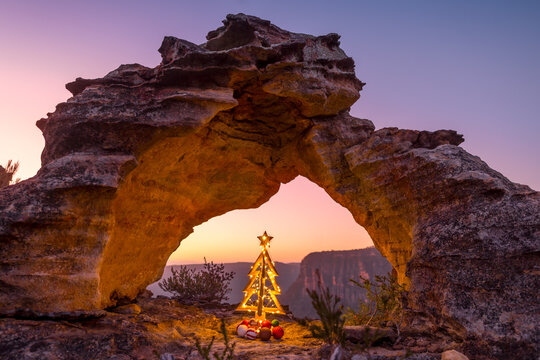 Rustic decorated Christmas tree on cliff ledge under arch Blue Mountains Australia