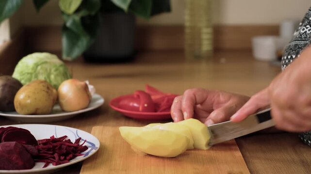 Cutting peeled potato into pieces for Ukrainian borscht. Chopping tuber preparing filling for national soup of Ukraine. Slicing fresh potato making essential ingredient for traditional Slavic dish