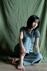 Obraz premium Person sitting on the floor against a green backdrop, wearing casual clothes and looking thoughtfully down
