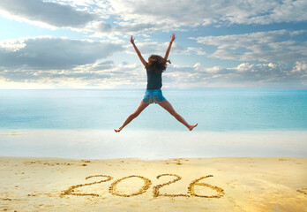 New Year 2026 written on sand, happy girl with hands up jumping on the beach