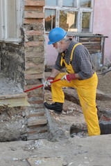 Adult worker demolishing old building wall using crowbar tool