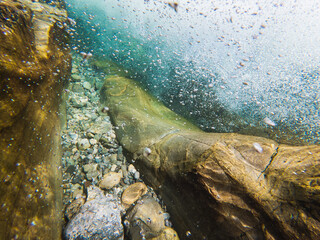 Dynamic underwater scene in a clear, cold Norwegian mountain river shows turbulent water, oxygen bubbles, and a rocky gravel riverbed.