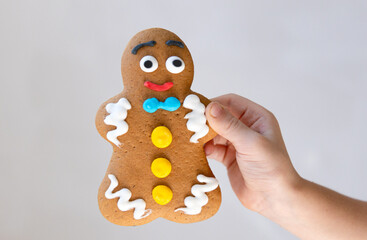 Close up of a gingerbread man cookie held in a child hand on light background with copy space. Sweet holiday concept for Christmas or childhood theme.