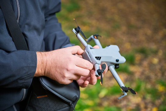 A person adjusts a drone in a lush forest filled with colorful autumn leaves on a calm afternoon. The passion for aerial adventure is evident in this moment.