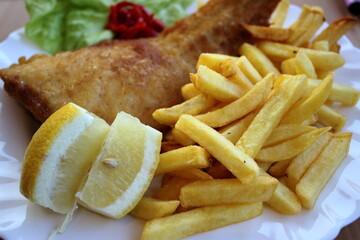 Fried fish and chips with lemon on white plate