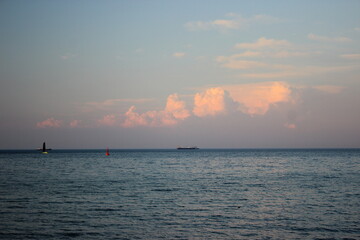Calm sea horizon with ships and pink clouds at sunset