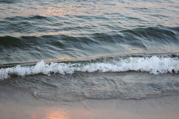 Sea wave washing sandy beach at sunset