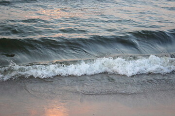 Sea wave washing sandy beach at sunset