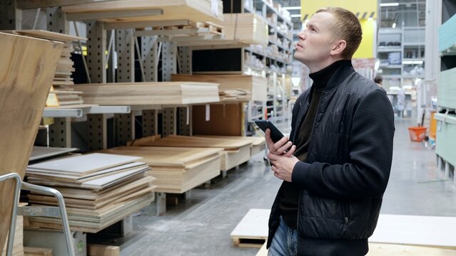 Contractor using his smartphone to plan a renovation project and select materials in a bustling lumber yard, while working with industry professionals