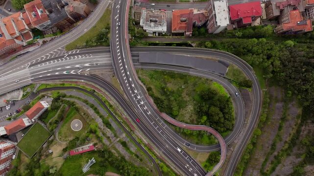 Top down aerial view of traffic on a highway interchange transitioning to La Salve Bridge over the Nervion river, revealing Guggenheim Museum