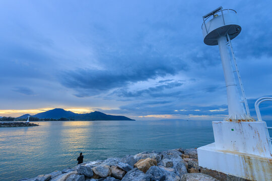 Lighthouse is on a rocky shoreline with a cloudy sky in the background