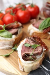 Bruschettas with roast beef, cream cheese, basil, sun-dried tomato and fresh vegetables on table, closeup