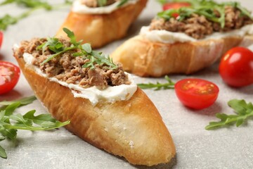 Delicious bruschettas with tuna, tomatoes and arugula on grey table, closeup