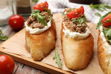 Delicious bruschettas with tuna, cream cheese and tomatoes on wooden table, closeup
