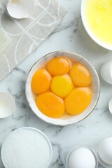 Raw eggs, yolks, whites and sugar on white marble table, flat lay