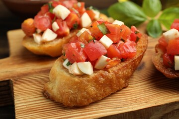 Tasty bruschettas with tomatoes, mozzarella cheese and basil served on wooden table, closeup