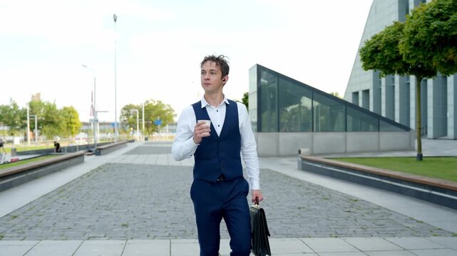 Young man walks outside, holding coffee, looking confident and focused