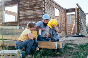 Family with young children wearing helmets near wooden house under evening sunlight