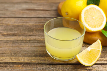 Lemon juice in glass, leaves and fresh lemons on wooden table, closeup. Space for text