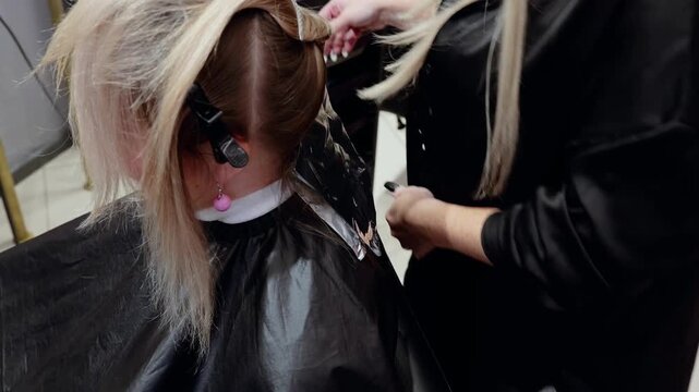 Highlighting hair professionally, Stylist applying bleach with foils, Closeup of hair coloring process taking place, Salon technician carefully applying highlights with protective gloves