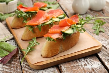 Tasty bruschettas with salmon, cucumber and arugula served on wooden table, closeup