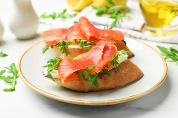 Tasty bruschettas with salmon and arugula served on white marble table, closeup