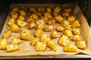 Roasted potato wedges on baking tray with herbs and spices. Homemade oven baked potato slices on parchment paper. Tasty side dish for lunch or dinner. Interior of home oven.
