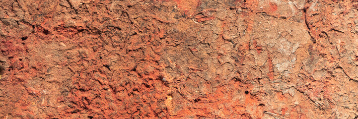 Real textured background of a dry cracked weathered red clay wall. For use concept of erosion, damage, and decay for abstract or grunge warm earth tone design themes