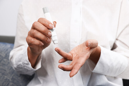 Diabetes. Woman checking blood sugar level with lancet pen indoors, closeup