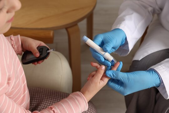 Diabetes. Doctor in medical gloves checking little girl's blood sugar level with lancet pen and glucometer indoors, closeup