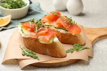 Tasty bruschettas with salmon, cream cheese, cucumber and arugula on grey table, closeup