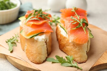 Tasty bruschettas with salmon, cream cheese, cucumber and arugula on table, closeup