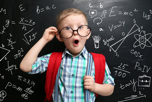 Cute little child in glasses near black chalkboard with formulas and drawings - Powered by Adobe